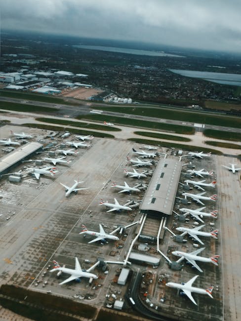 This image shows an aerial view of Heathrow Airport's Terminal 5, featuring numerous British Airways aircraft parked on the tarmac, connected by jet bridges to the terminal building. The aircraft are