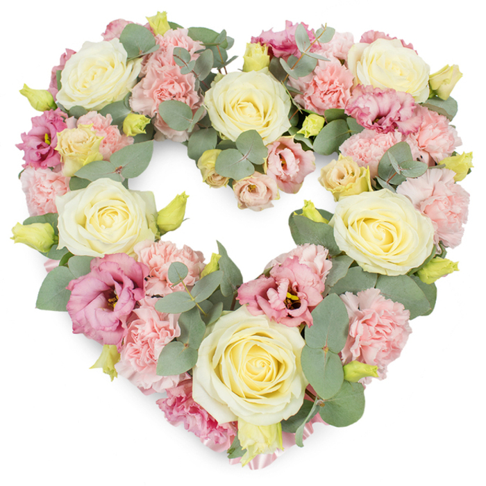 A beautifully composed, heart-shaped floral tribute fills the frame, set against a clean white background so that every petal and leaf can be clearly distinguished. The heart itself is lush and perfectly formed, its curves smooth and symmetrical, suggesting a steady, practiced hand. Dominating the design are creamy ivory and pale yellow roses, spaced evenly to create visual anchors across the composition. Their densely layered petals form rounded, velvety blooms that convey refinement and composure. Between these roses, soft pastel pink carnations are nestled, their frilled edges and clustered form adding volume and a gently textured surface to the heart. Deeper pink to mauve lisianthus blossoms are threaded through the arrangement, some partially open and others fully unfurled, providing a slightly looser, more relaxed shape that contrasts gracefully with the tighter roses and carnations. Cooling the palette, silvery-green eucalyptus foliage winds delicately around the blooms, its rounded leaves and matte texture offering a calm counterpoint to the more luminous petals. Here and there small yellow-green buds emerge, adding tiny sparks of vitality and hinting that life continues even amidst farewell. This wreath feels very much like a piece crafted for a Harmondsworth family saying goodbye in a village church or at a nearby crematorium, where understated beauty is often preferred. The white backdrop heightens the sense of purity and allows the pastels to glow softly without distraction. Overall, the arrangement communicates a message of love, remembrance, and sympathy in a quiet, dignified manner, suitable for delivery to services or homes throughout Harmondsworth and its surrounding lanes.